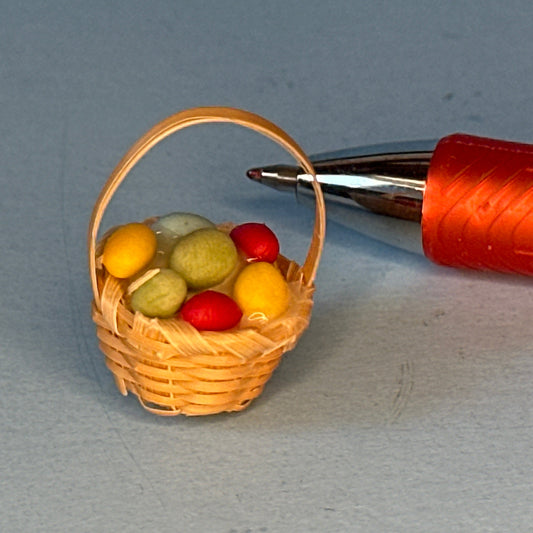 Miniature wicker basket with colorful balls next to a pen on a gray background