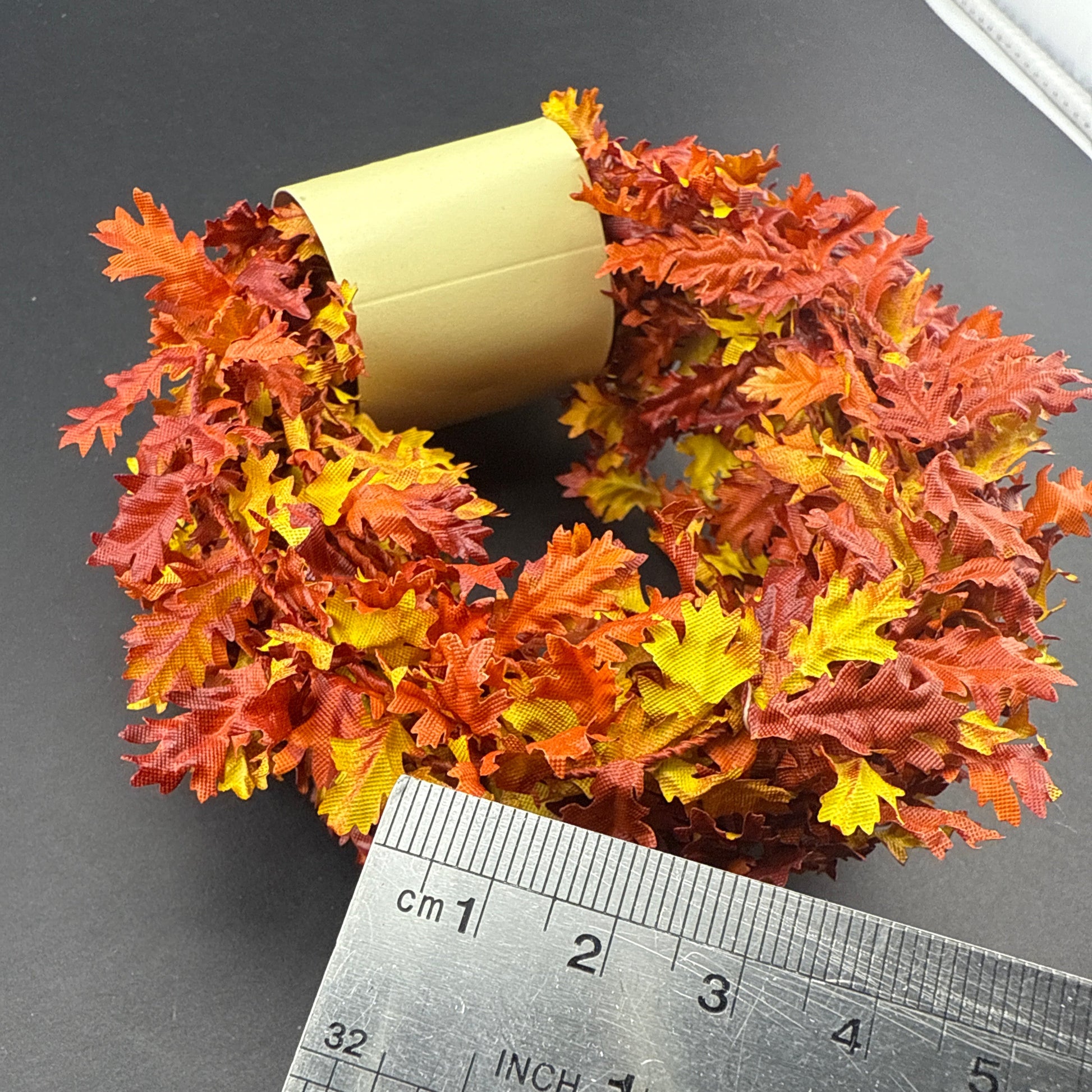 Decorative wreath with autumn leaves next to a ruler on a dark surface