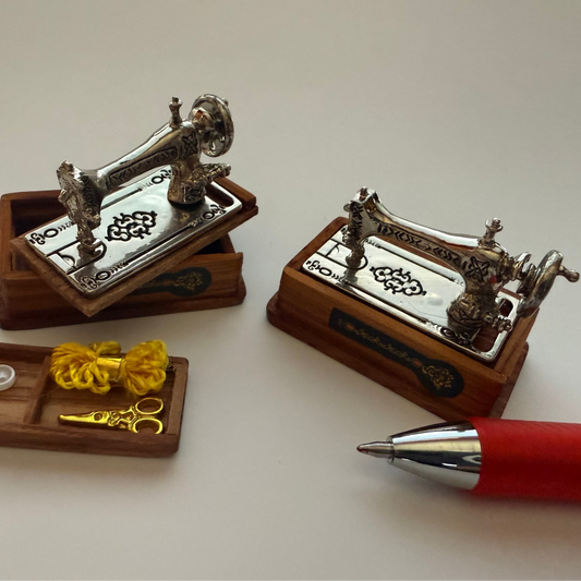 Miniature sewing machine models on a white background with a pen for scale.