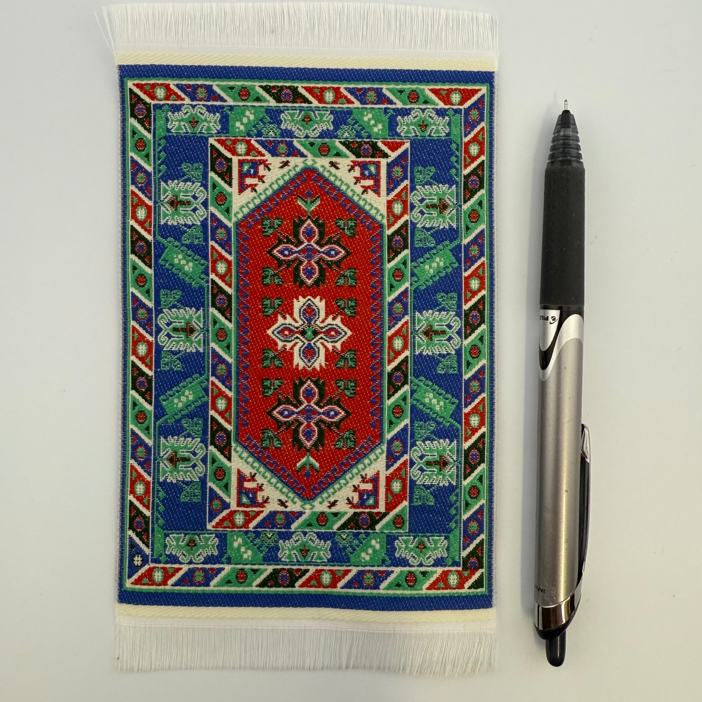 Decorative rug with geometric pattern next to a pen on a white surface