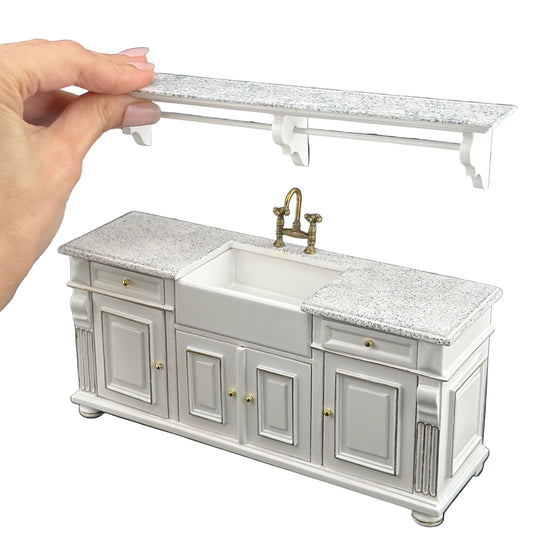 Hand holding a miniature kitchen cabinet model with a sink and faucet against a dark background