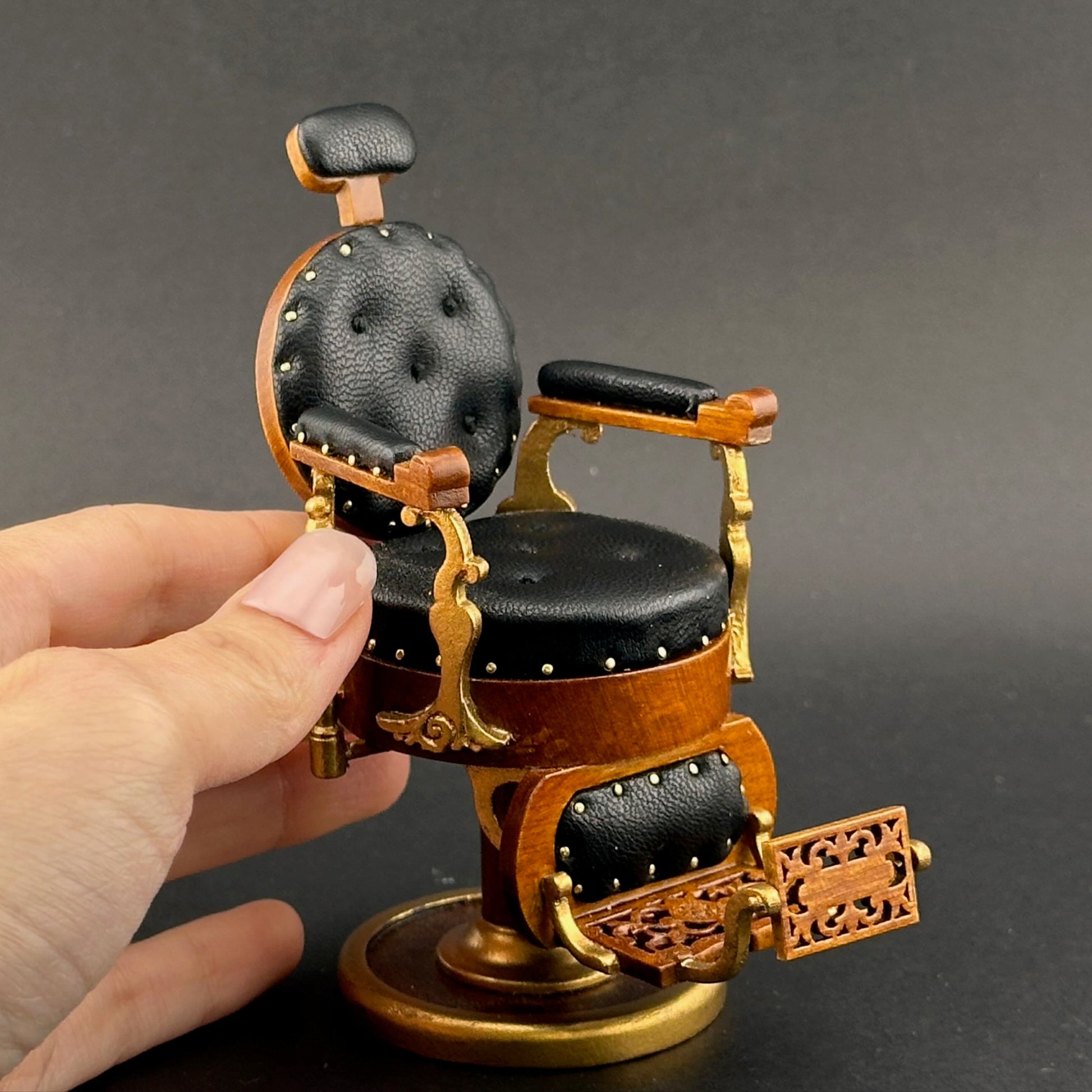 Small model of a barber chair held in a hand against a dark background