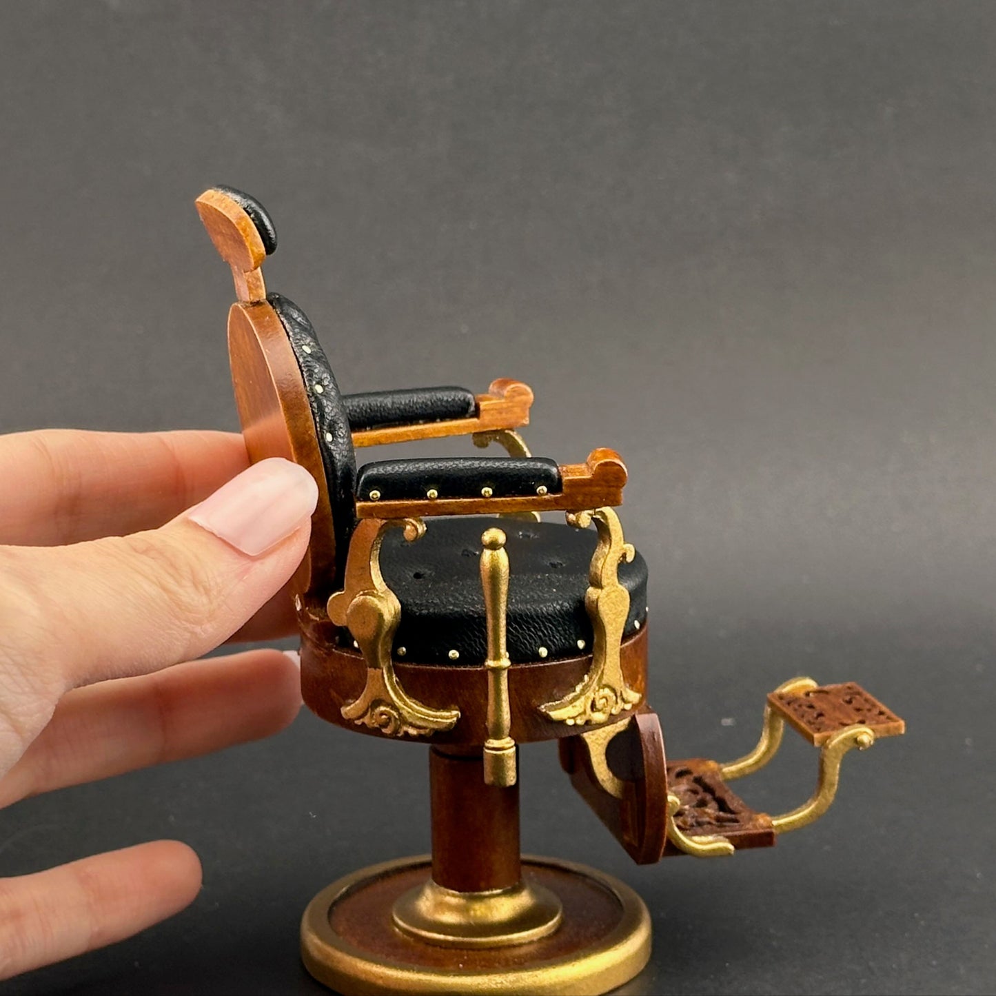 Hand holding a miniature barber chair model against a gray background
